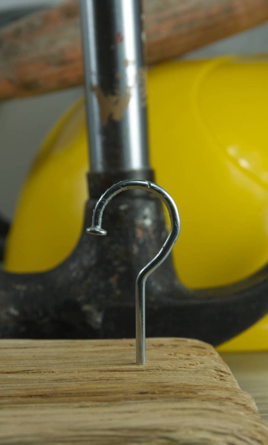 Construction nail shaped as question mark with blurred background of various tools and helmet, construction questions and confusion concept